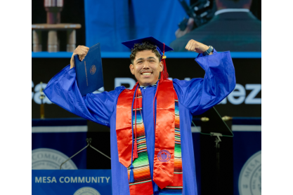 2025 graduate in a show-your-muscles pose on stage during the commencement ceremony. 