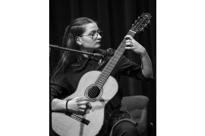 Person with long dark hair playing a guitar with the arm pointing upward. 