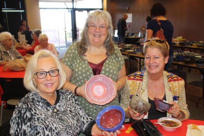 Three happy women posing with their ceramics bowls during a 2015 MCC Empty Bowls event.