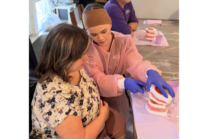 A dental hygiene student demonstrating tooth brushing techniques, using  typodont model, a life-sized, anatomically accurate representation of the human mouth, to a community member. 