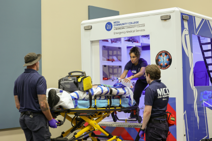 MCC students and faculty loading a mock patient into the back of an ambulance simulator. 