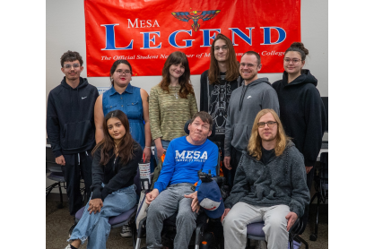 Nine journalism students standing in front of a Mesa Legend banner. 