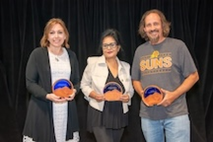 Maralena Cicchetti, Rupanjana Sengupta and Czar Goetz in front of a black curtain; each is holding a round plaque of wood and glass with a desert landscape and a Saguaro cactus. The plaques have the words 2026 Outstanding Adjunct Faculty, their name and Mesa Community College. 