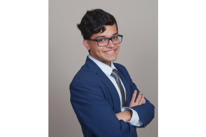 Pranay Modha, a smiling young man with short dark hair wearing dark rimmed glasses and a blue suit with a tie. 