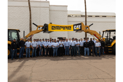 Group of students earning Associate in Applied Science degrees while participating in Empire Southwest’s ThinkBIG apprenticeship program between two large pieces of machinery holding up an Empire CAT banner. 