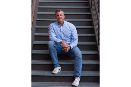 Travis Webb, LCSW, wearing a light blue dress shirt and jeans, sitting on stairs