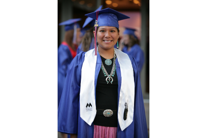 Smiling woman wearing Native American jewelry and cap and gown.