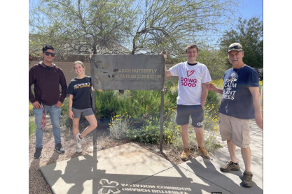 Three people posing by a tall Monarch Butterfly Waystation Corridor sign. 