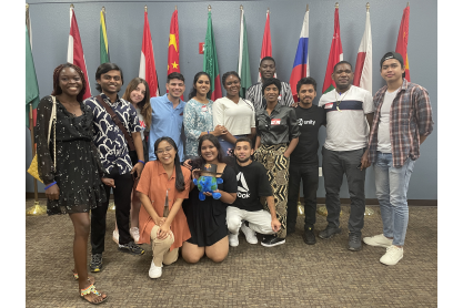 Group of students in front of flags from various countries smiling at camera.