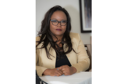Dr. Tammy Robinson, sitting at a table. She has long dark hair and is wearing dark rimmed glasses and a beige suit jacket.