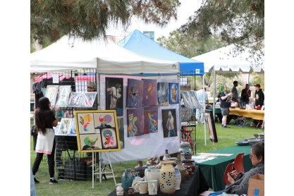 Booths outside with colorful paintings and a woman looking at a painting