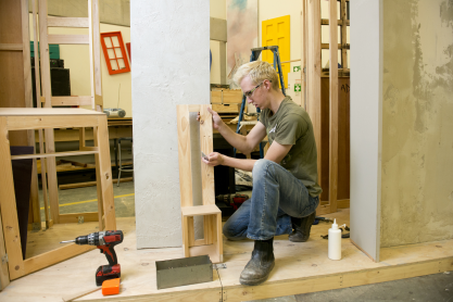 Person working with wood and a ruler in a workshop. 
