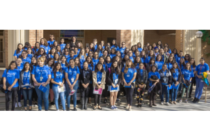 A large group of people in royal blue t-shirts posing along with a couple of executives. 