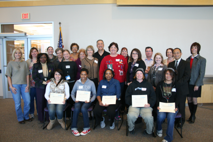 A group poses for the camera with four in front holding certificates.