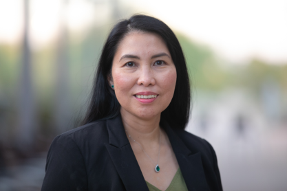 Head and shoulders photo of a woman with long straight black hair, parted on the side, wearing a black jacket. 