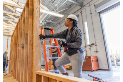 Woman wearing a hard hat, constructing a wall frame. 