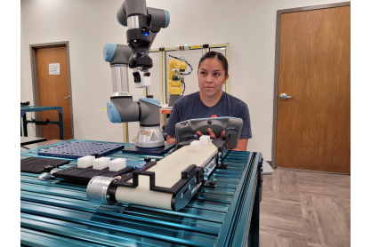 Woman with dark hair pulled back operating a small robotic arm to perform a function. 