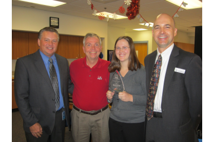 Michelle Barton holding a glass award and posing with three people.