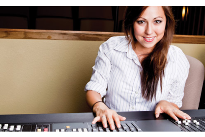 A woman with long dark hair, wearing a striped blouse, with her hands on a music mixer board. 