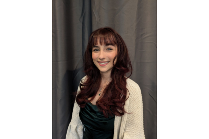 Young woman with long, dark brown hair, white sweater and black blouse smiling