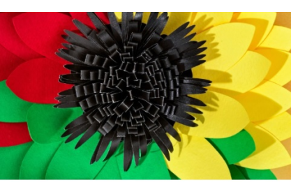 A green, red, yellow paper flower with a black center. 