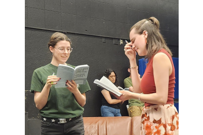 Two women rehearsing a play scene. Both are holding books.