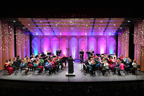 Both Desert Echoes Flute Project flute choirs on stage split into two halves right and left with pretty pink and purple stage lighting