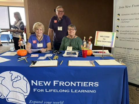 Three people sitting at a table with a blue New Frontiers tablecloth
