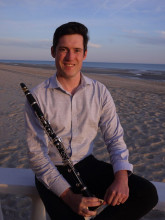 Clarinetist Riley Braase pictured with clarinet at a beach with water in the background