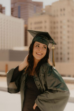 Abbygale Gurr, girl with long dark hair wearing green graduation gown and cap, looking over her shoulder. 
