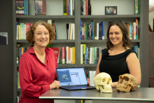 Dr. Annalisa Alvrus and Laura Ballard standing behind counter with laptop and two human skull replicas. 