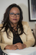 Dr. Tammy Robinson, sitting at a table. She has long dark hair and is wearing dark rimmed glasses and a beige suit jacket.