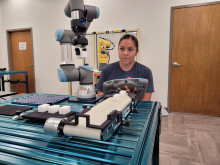 Woman with dark hair pulled back operating a small robotic arm to perform a function. 