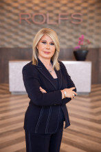 Francis Tesmer in a black suit posing in her salon with ROLFS logo behind her.