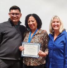 Man in grey shirt, Tawn Haupti displaying her certificate and a woman in a navy blue blouse. 