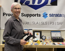 Pam Waterman in a grey shirt next to a display of 3D printed items.