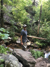 Mike Rague standing by a stream in a wooded forest. 