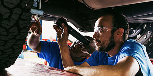 Two students inspect the underside of a car.