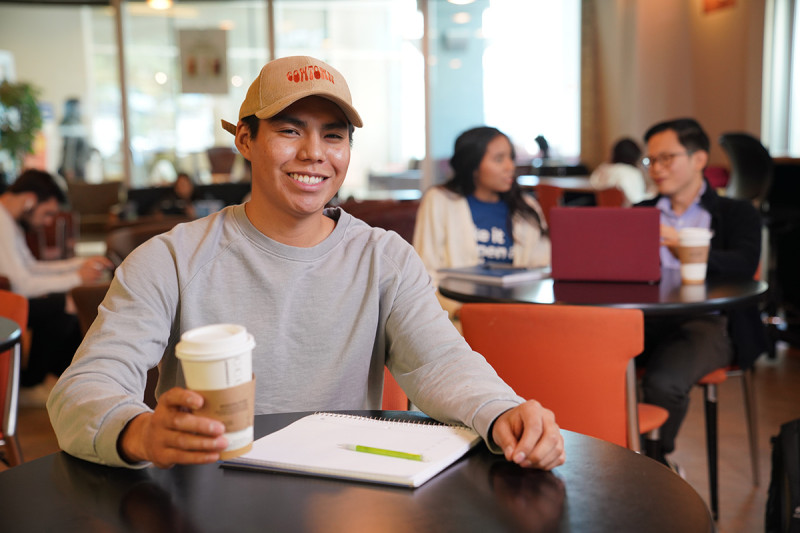 A student at a table holding a cup of coffee.