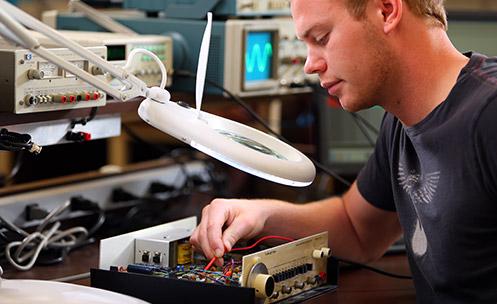 A person using a large magnifying glass to work on electronics.