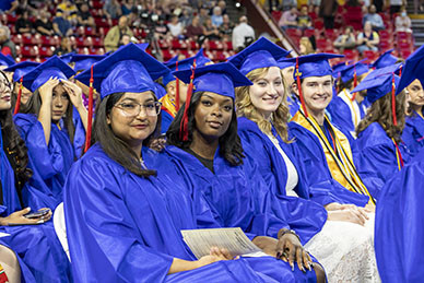 Four graduate seated in a row at the graduation ceremony.