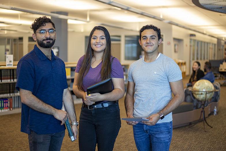 Three students standing in the campus library.