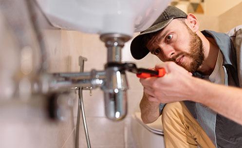 A plumber using a wrench under a sink.
