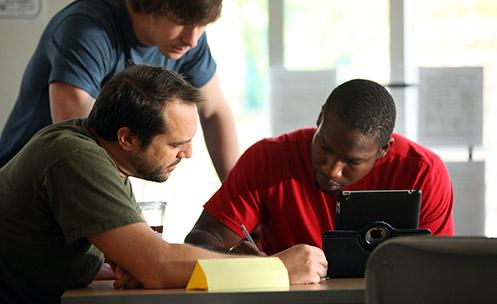 Three people looking at a tablet on a table.