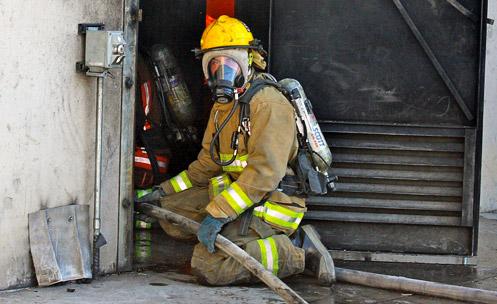 A firefighter in full uniform kneeling and holding a hose.