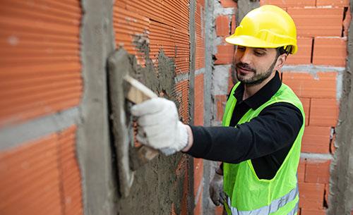 A person in construction gear smoothing over a cement wall.