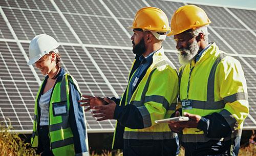 Three people wearing hard hats in front of solar panels.