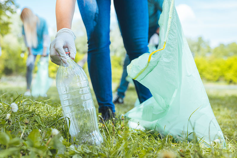 Picking up a bottle from the grass while holding a trash bag.