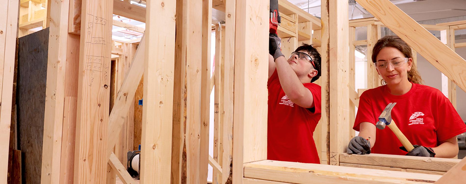 Two students with a hammer and saw work on framing a wall.