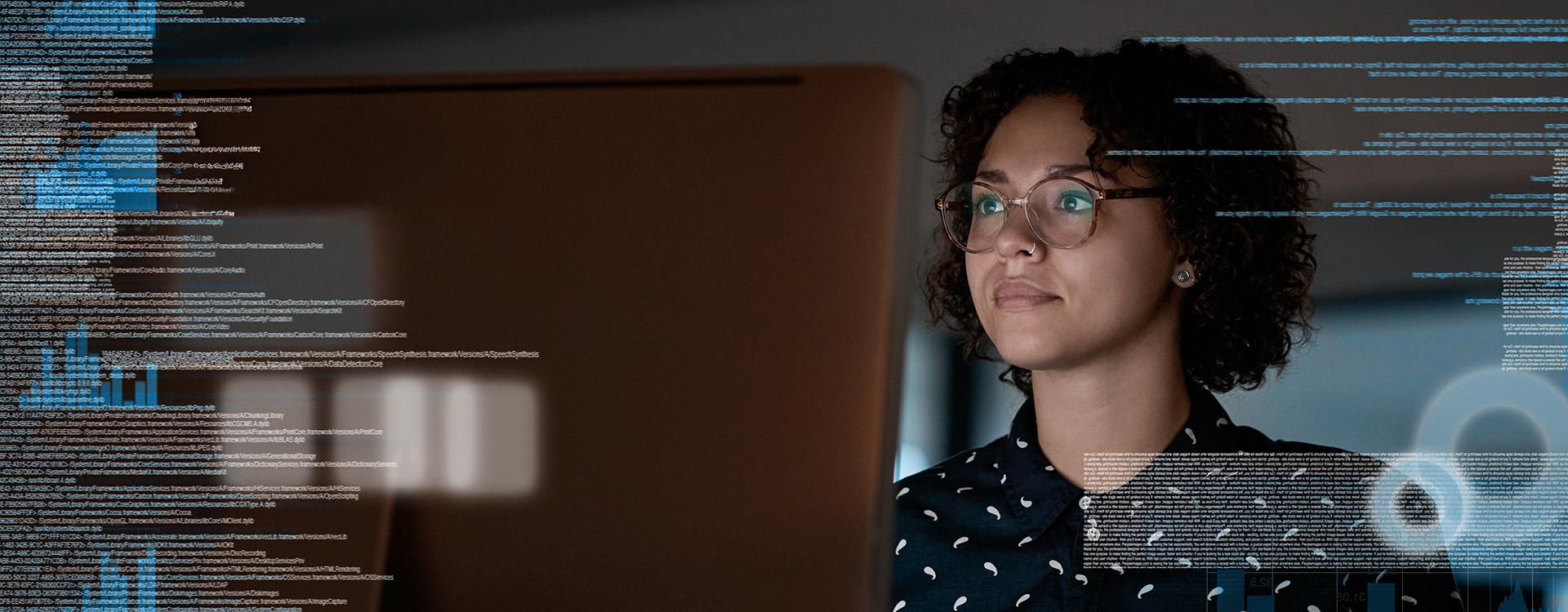 A person looking at a desktop monitor with graphs and code to the sides.